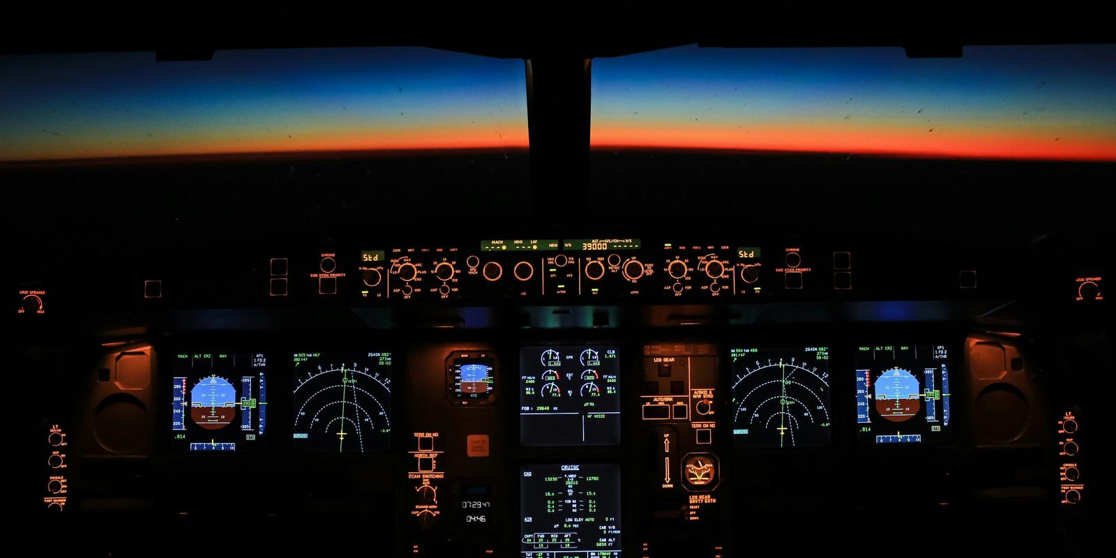 An airliner cockpit at night with glowing instruments and a sunrise on the horizon