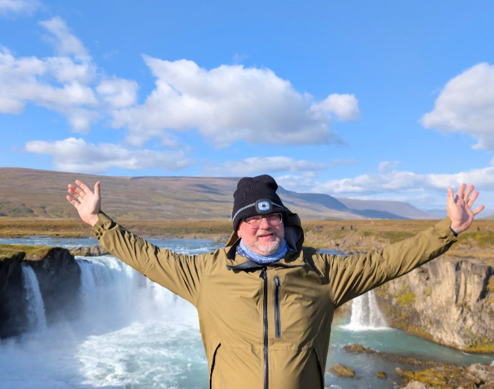 Dennis Jöst with arms spread wide like wings in front of a waterfall in Iceland